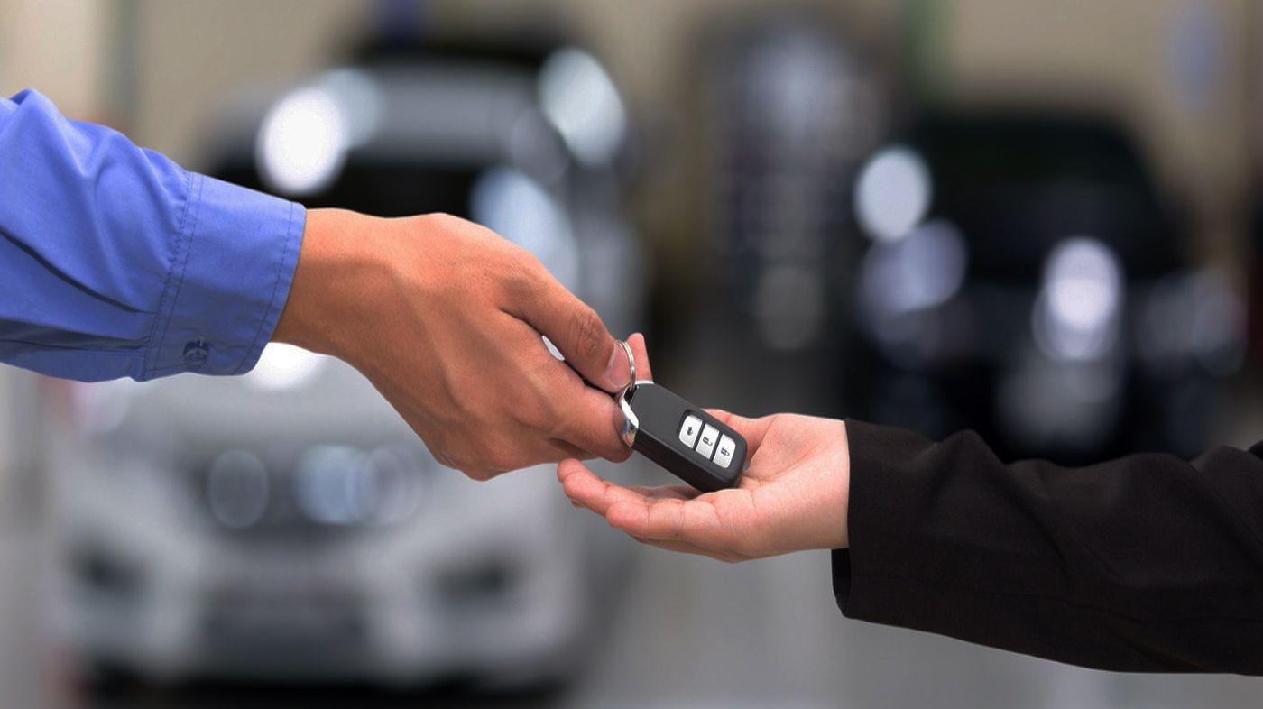 Close-up of one person handing over car keys to another person with cars blurred in the background.